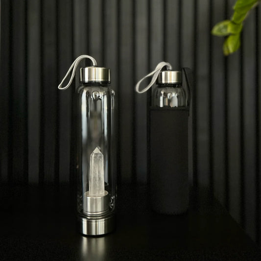 Clear Quartz Crystal Water Bottle by The Goddess Collective, featuring a natural crystal obelisk inside a glass bottle with stainless steel lids and carry sleeve.