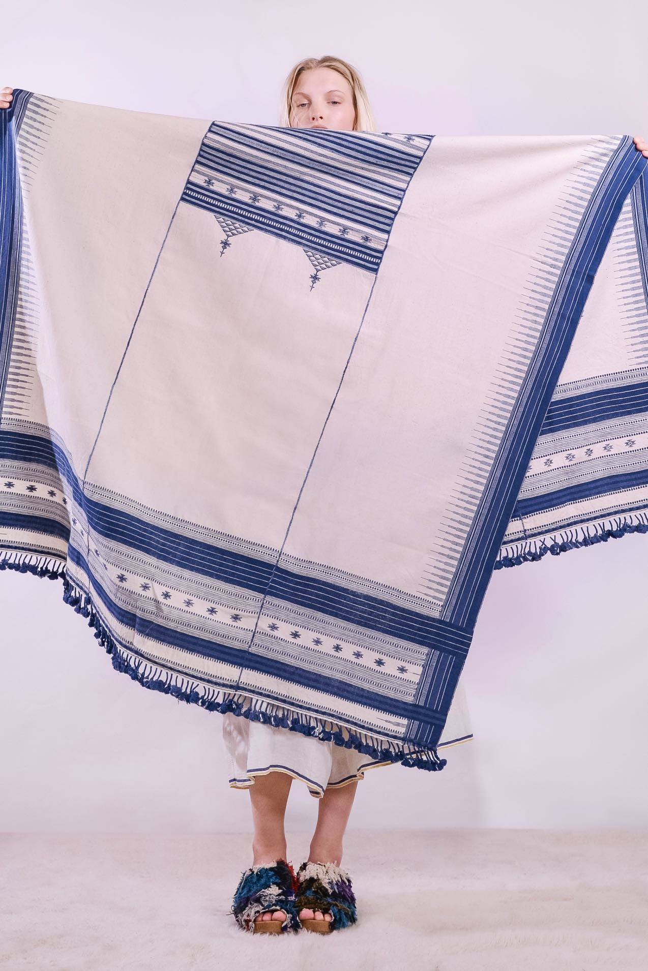 Handwoven kala cotton throw with embroidered panels by Shamji Vankar Vishram Valji, crafted in Bhujodi, India. Made from handspun yarn for a rich, textured feel. A heritage piece curated by House of Woven Stories, blending tradition, sustainability, and artisan craftsmanship. Available at House of Woven Stories.