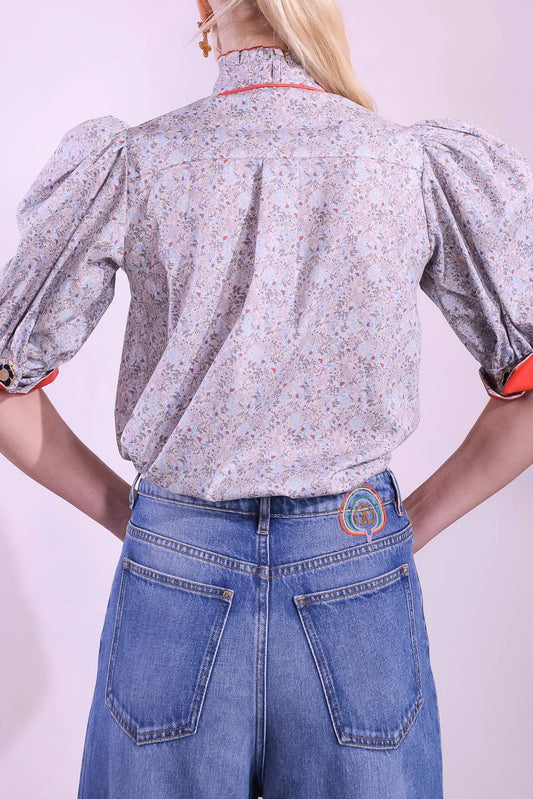 Model is wearing the Mirca Fantasia Liberty Blouse by House of Woven Stories: a lightweight cotton blouse with Liberty floral print, puffed sleeves, bright coral trims, a vintage collar button, and a matching fabric tie for styling.