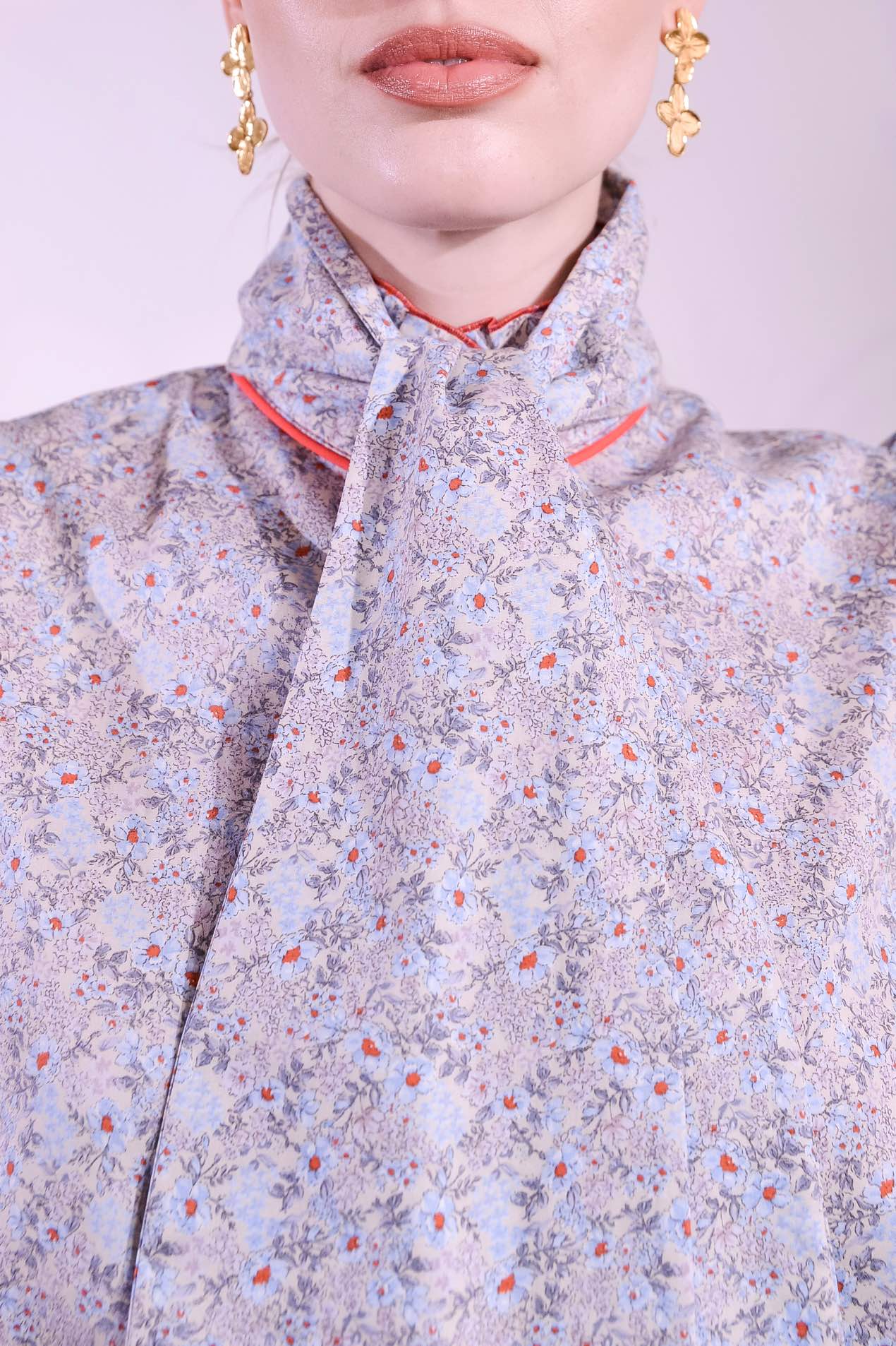 Model is wearing the Mirca Fantasia Liberty Blouse by House of Woven Stories: a lightweight cotton blouse with Liberty floral print, puffed sleeves, bright coral trims, a vintage collar button, and a matching fabric tie for styling.