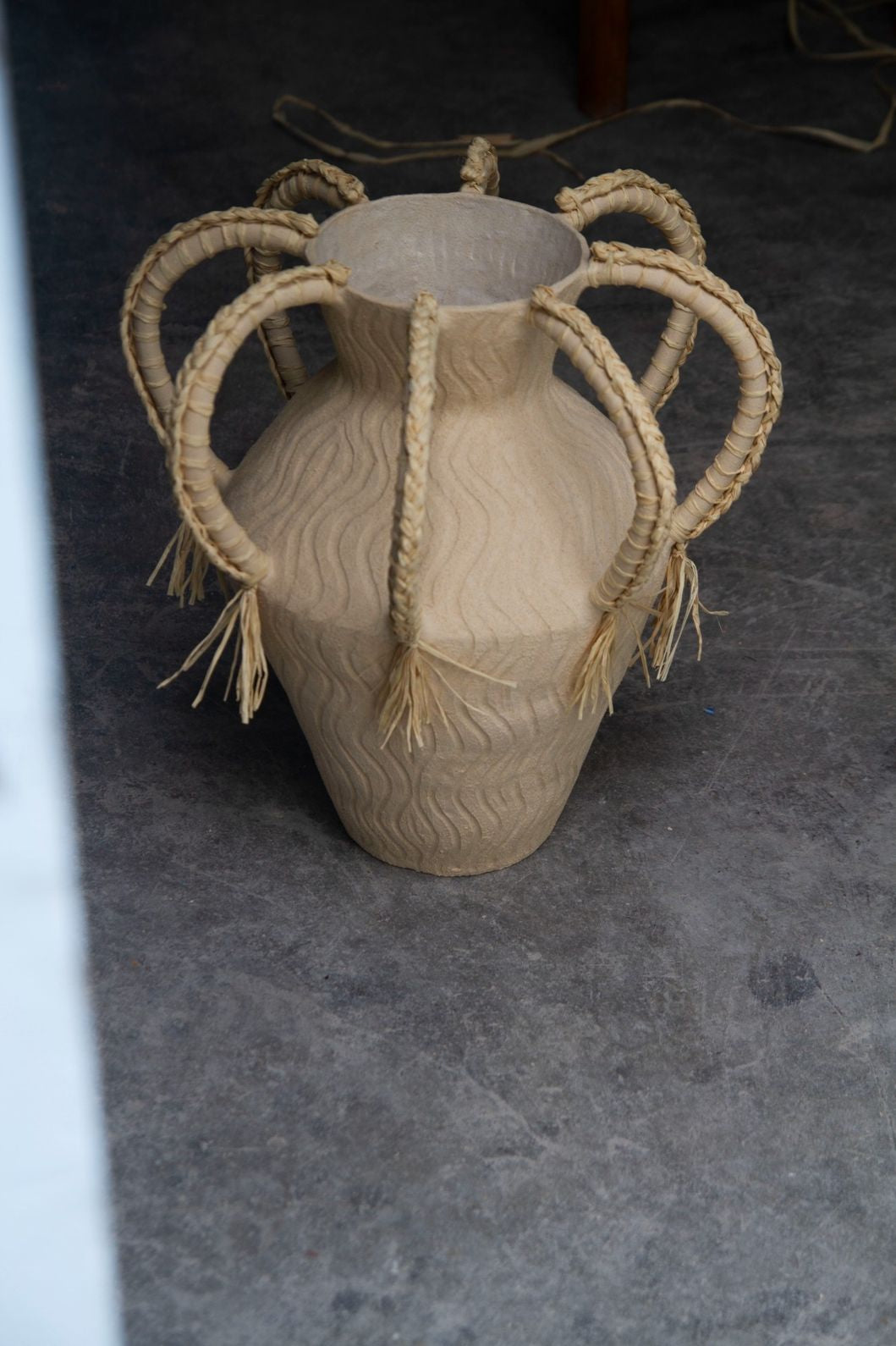 Amphora Ondas by Clandestine Céramique, handbuilt in sandy clay with engraved wave patterns and eight braided raphia handles, part of the House of Woven Stories selection.
