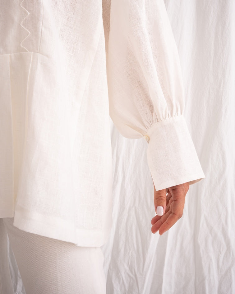 Model is wearing the Ancestral White Linen Shirt by Les Vacances d’Irina, a unisex handmade linen shirt with relaxed cut, open V-neckline, and natural shell buttons, crafted in Bucharest and available at House of Woven Stories.