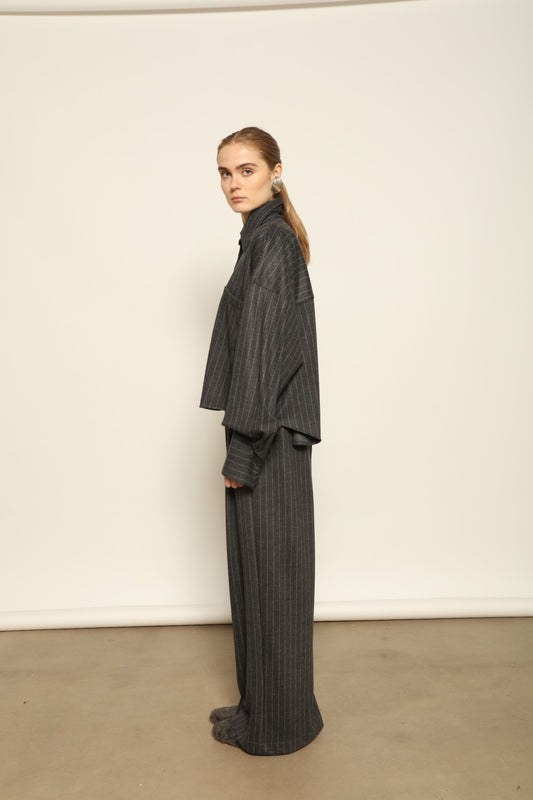 Model is wearing Bettina Striped Grey and White Double Jersey Shirt by House of Woven Stories, part of the curated selection, handcrafted in Italy from linen, wool, and silk blend with vertical stripes, relaxed tailoring, and fluid drape for timeless elegance.