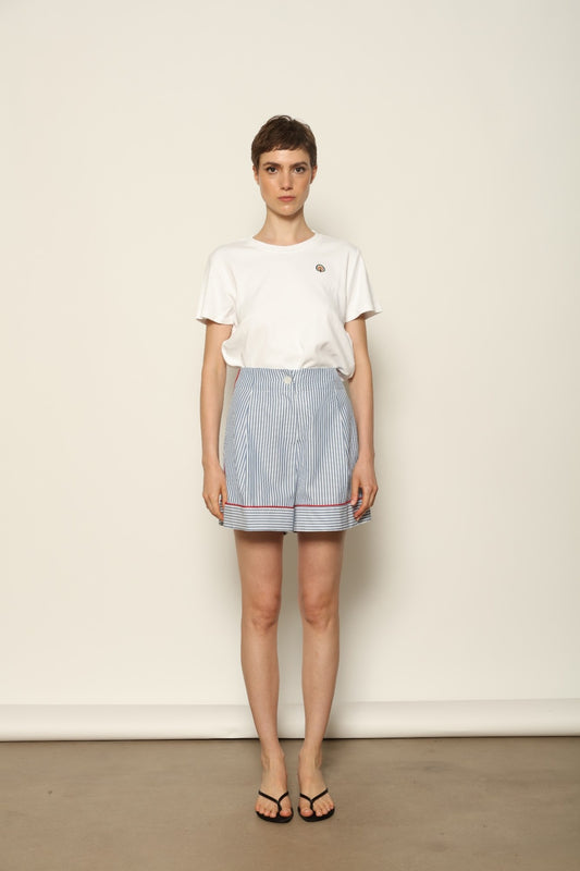 Model is wearing blue and white striped 100% cotton shorts with contrasting red piping by House of Woven Stories. The shorts feature a relaxed, tailored silhouette designed for comfort and ease of movement. Made in Italy from premium natural cotton, they reflect artisan craftsmanship and timeless warm-weather style, styled as part of a contemporary resort wear look.