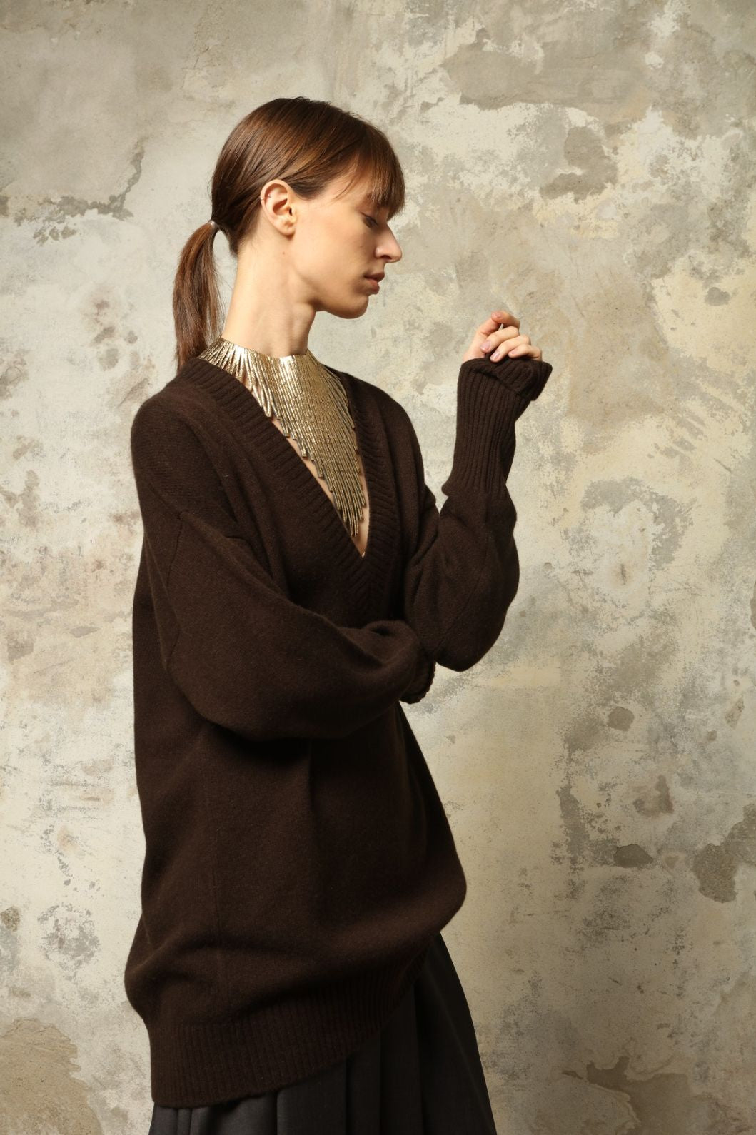 Model is wearing the Chocolate Nina V-Neck Long Sweater by House of Woven Stories, crafted from 100% pure Inner Mongolia cashmere in a deep chocolate shade, featuring an elongated silhouette, deep V-neckline, soft breathable knit, and timeless sustainable Italian luxury design