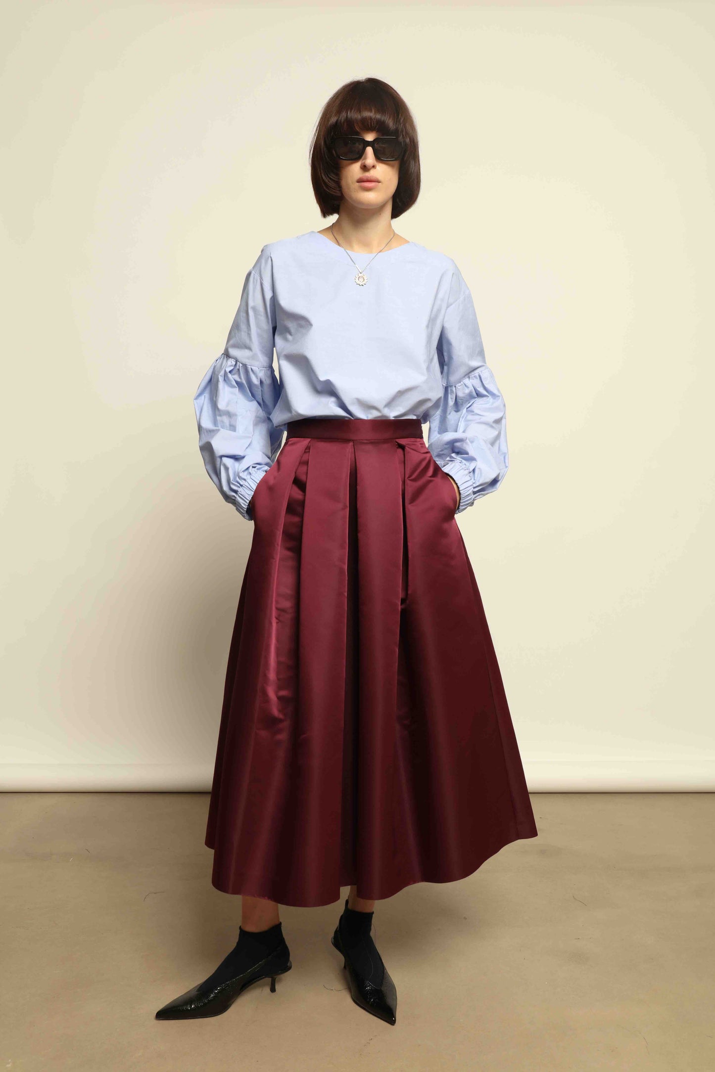 Model is wearing the Duchesse Violet Skirt by Lunatica Milano in mirtillo purple with box pleats and a flowing, elegant silhouette.