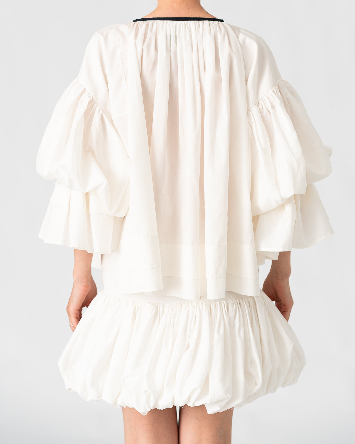 Model is wearing the Favignana Cotton and Silk Blouse by Les Vacances d’Irina, a vintage-inspired handmade blouse with pleated three-quarter sleeves, black bow neckline, and luxurious cotton-silk fabric, available at House of Woven Stories.