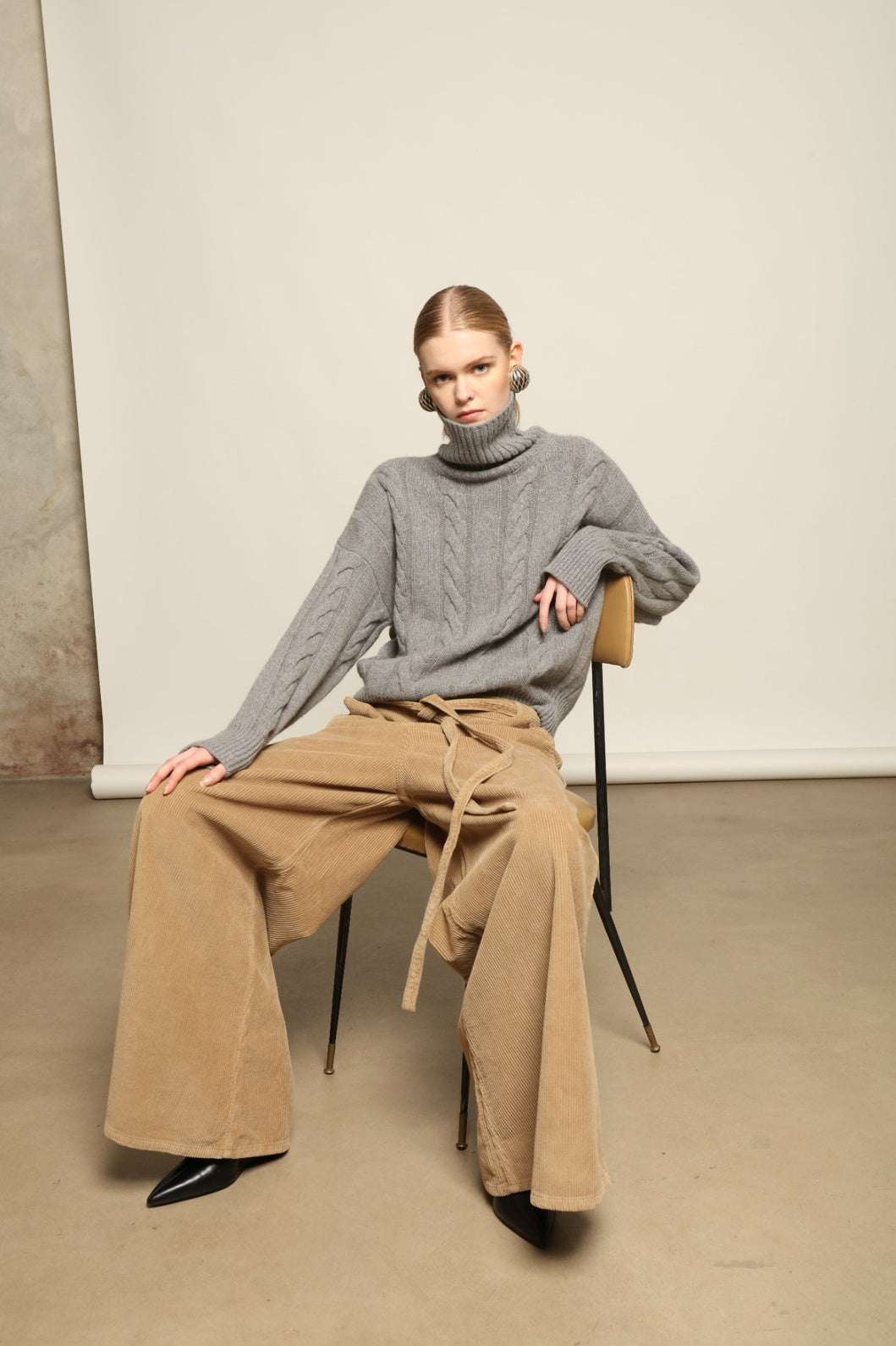 Model is wearing Le Pantalon Over Chino in Beige by Happy Haus, flared oversized corduroy cotton trousers with removable belt, corozo buttons and peacock embroidery, curated in the House of Woven Stories selection.