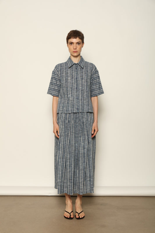 Model wearing the Emily Blue Striped Ikat Shirt by House of Woven Stories, crafted from 100% hand-loomed Kala cotton with indigo stripes, artisanal ikat pattern, and a relaxed cropped silhouette.