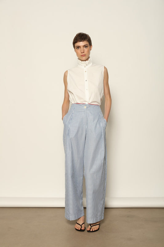 Model wearing the Gabriella Blue & White Striped Trousers by House of Woven Stories, featuring 100% cotton fabric, blue and white stripe pattern, relaxed fit, and contrasting red piping at the waistband.
