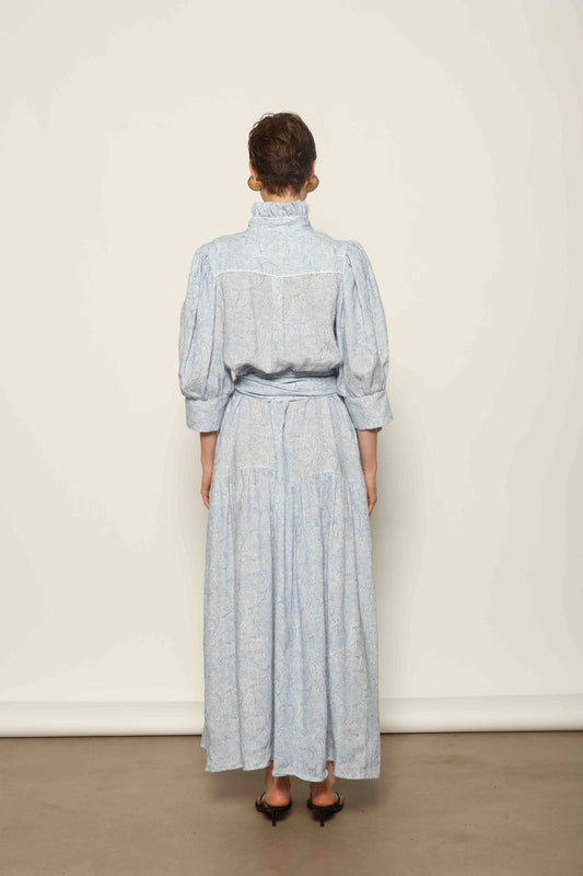 Model wearing the Karin Blue Paisley Dress by House of Woven Stories, featuring 100% linen fabric, soft blue paisley print, and a relaxed flowing silhouette with breathable lightweight structure.
