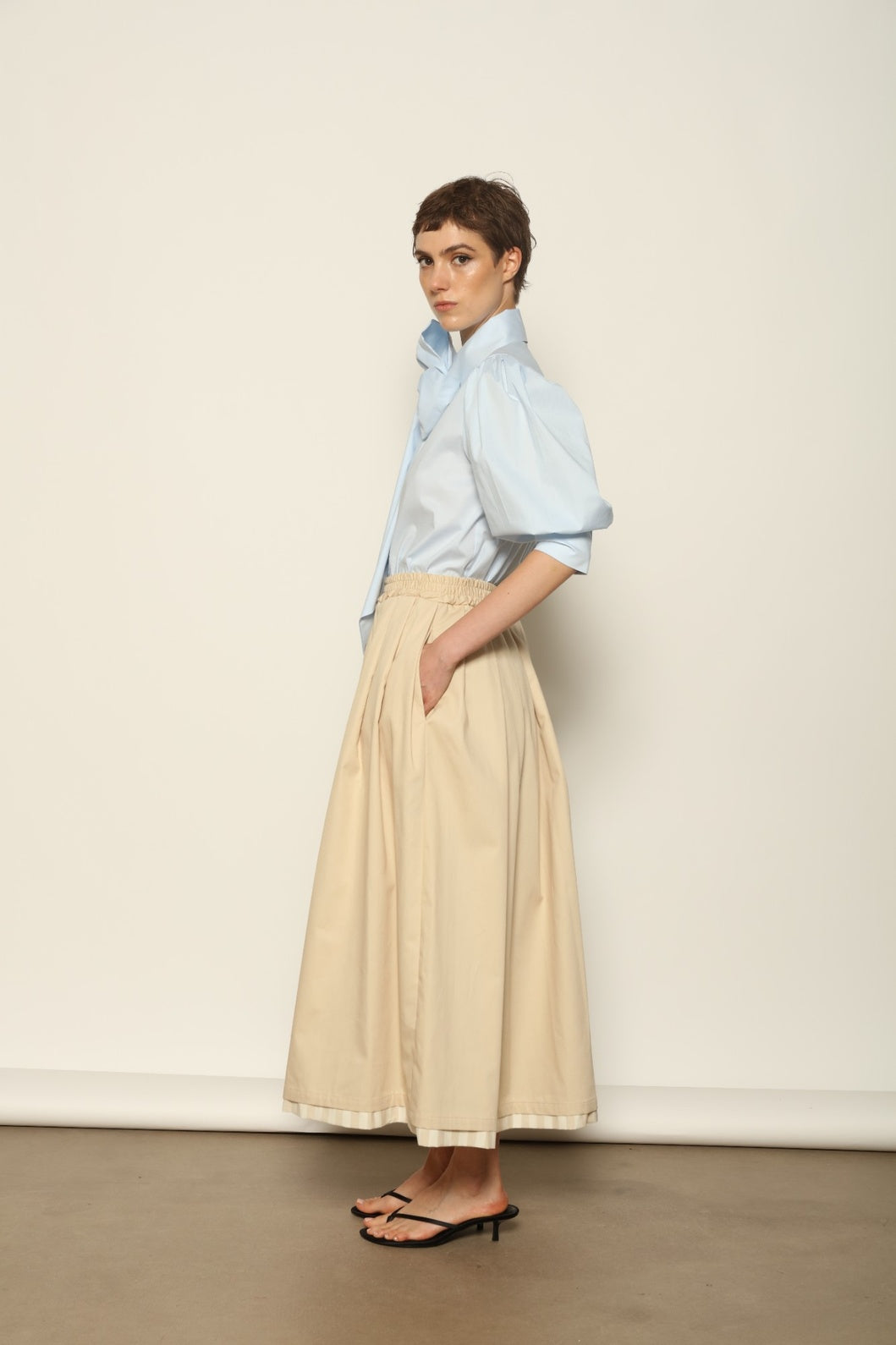 Model wearing the Seoul Camel Skirt by House of Woven Stories, featuring a structured camel-toned fabric, high-waisted fit, and a clean tailored silhouette with defined architectural lines.