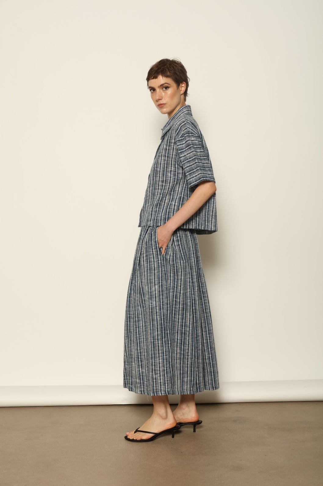 Model wearing the Seoul Indigo Blue Striped Ikat Midi Skirt by House of Woven Stories, crafted from handwoven Kala cotton with an indigo blue and off-white ikat pattern, elasticated waistband, and relaxed midi silhouette.