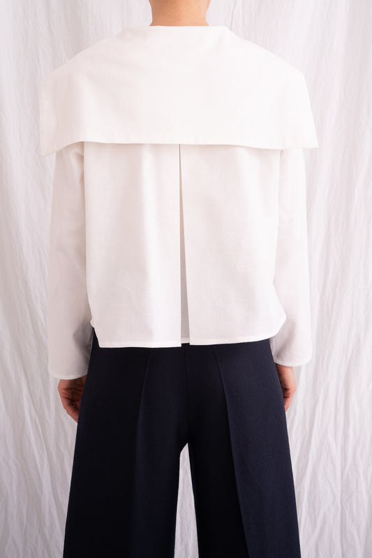 Model is wearing the Le Matelot White Blouse by Les Vacances d’Irina, a long-sleeved cotton blouse with sailor collar, handmade in Romania with artisanal detailing.