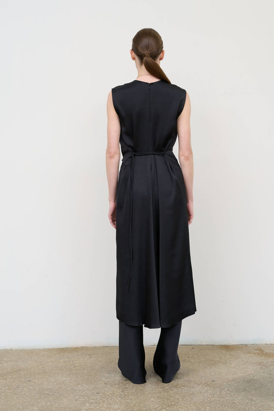 Model is wearing a black waist-twisted satin dress by Litkovska with sculptural twist at the waist and fluid silhouette, designer women’s dress available at House of Woven Stories