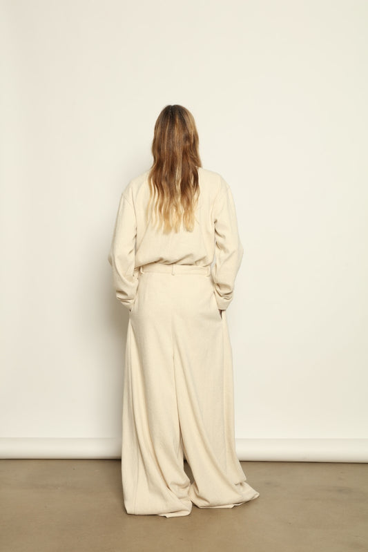 Model is wearing the Mid Rise Ecru Boucle Solid Pant by Marrakshi Life, part of House of Woven Stories collection, handwoven cotton boucle pants with mid-rise fit, front pleats, and wide flowing leg