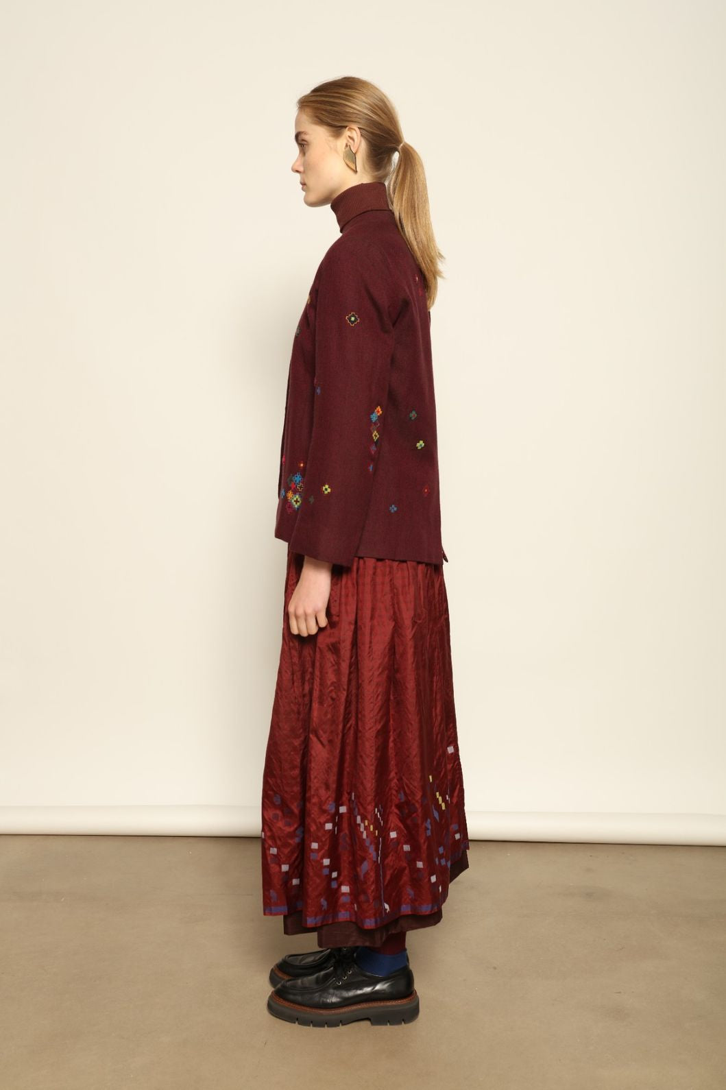 Model is wearing the Miraj 103 Silk Skirt by Injiri, handcrafted in red silk with vibrant rectangular motifs along the hem, blending artistry, movement, and refined elegance.