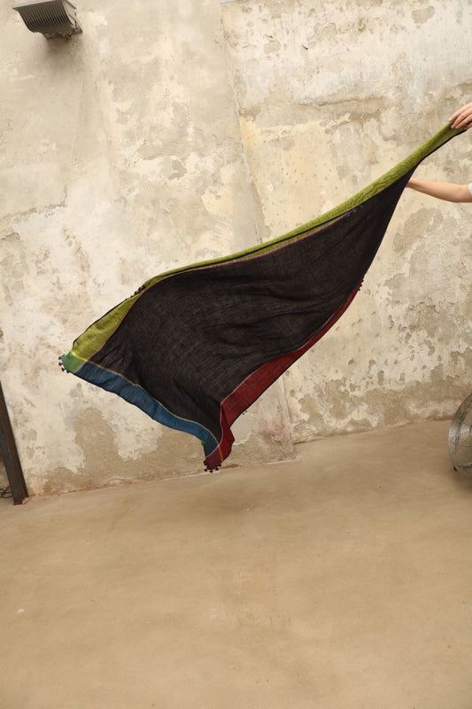 Model is wearing the Miraj 142 Cashmere Scarf by Injiri, handwoven from Himalayan cashmere with a dark base and rich indigo, turquoise, purple, brown, and green borders, combining warmth, softness, and artisanal elegance.