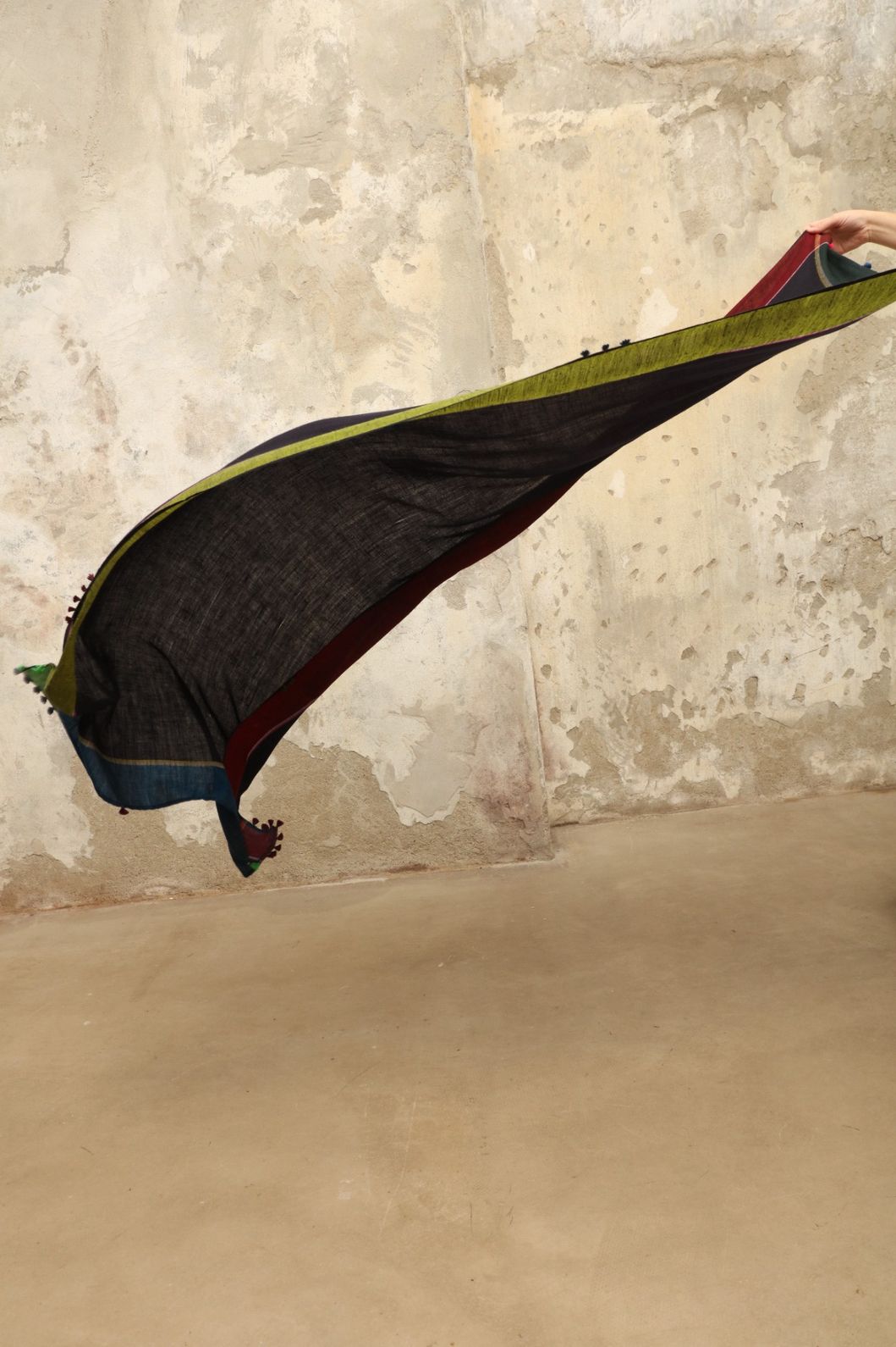 Model is wearing the Miraj 142 Cashmere Scarf by Injiri, handwoven from Himalayan cashmere with a dark base and rich indigo, turquoise, purple, brown, and green borders, combining warmth, softness, and artisanal elegance.