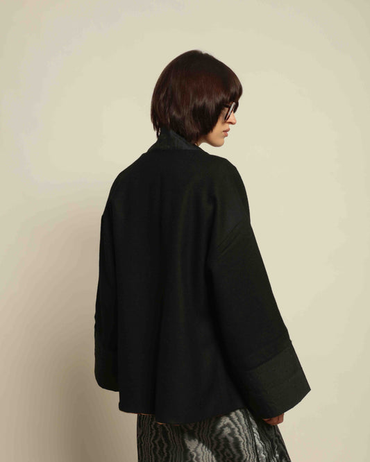 The model is wearing the Obidi Midnight Kantha Jacket in pure black, made of wool with a silk collar and Kantha silk lining, a timeless and versatile piece.