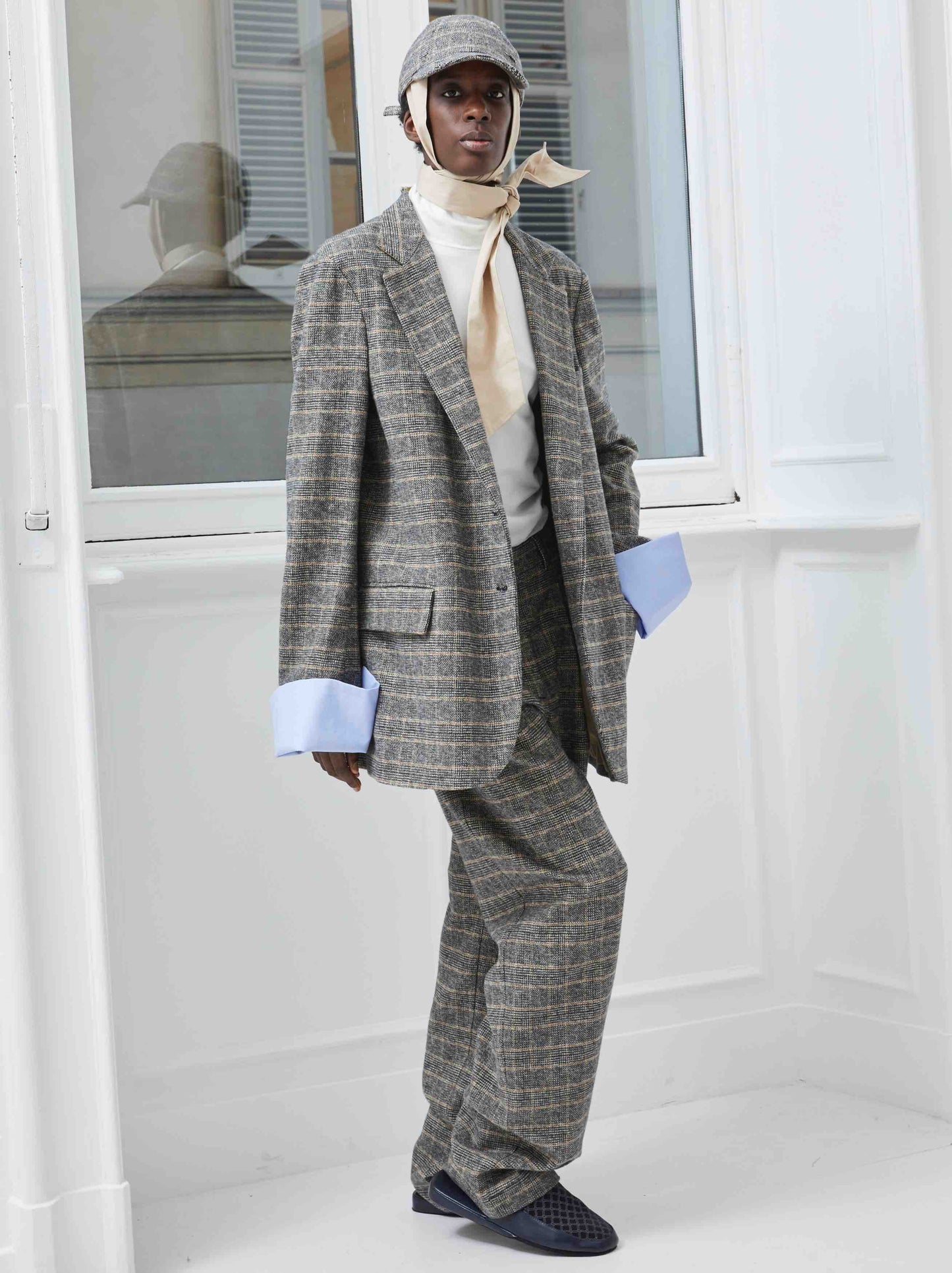 Model is wearing the Birkin Cotton Checked Blazer by Maison Jejia, part of the House of Woven Stories selection, featuring a grey checked pattern, notched lapel, and oversized blue cuffs.