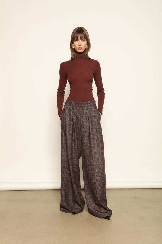 Model is wearing the Parigi Burgundy Lana Trousers by House of Woven Stories – Italian-tailored trousers crafted from a luxurious blend of merino wool, silk, and linen, featuring front pleats, side pockets, and a relaxed yet elegant burgundy silhouette.