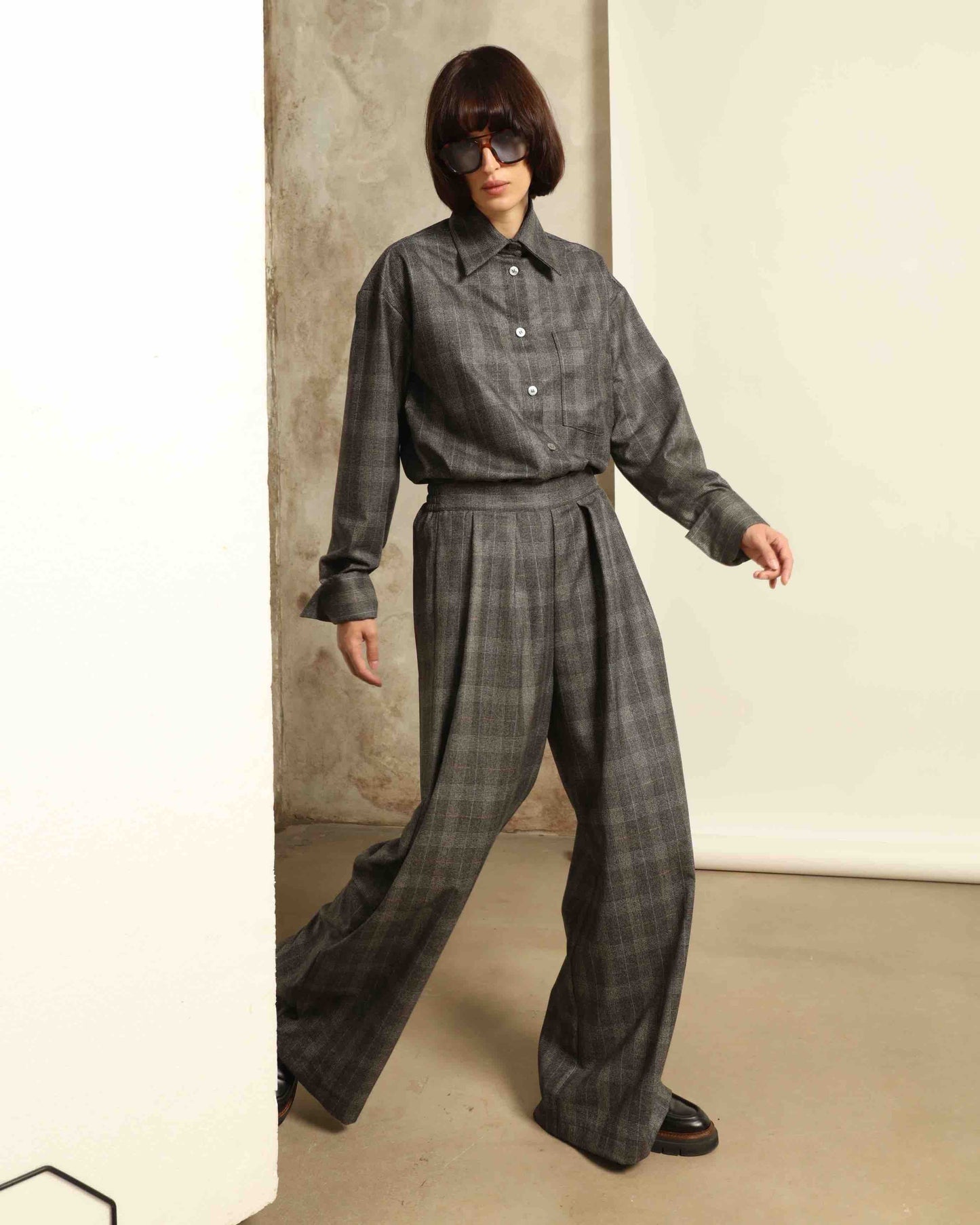 Model is wearing the Parigi Grey Check Trousers by House of Woven Stories, featuring a refined grey check pattern and a tailored silhouette, handcrafted in Piedmont, Italy.