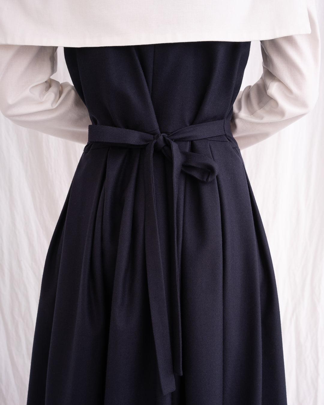 Model is wearing the Sarafan Pure New Wool Dress by Les Vacances d’Irina, a handmade navy merino wool dress with A-line silhouette, tie-back detail, horn buttons, and side pockets, available at House of Woven Stories.