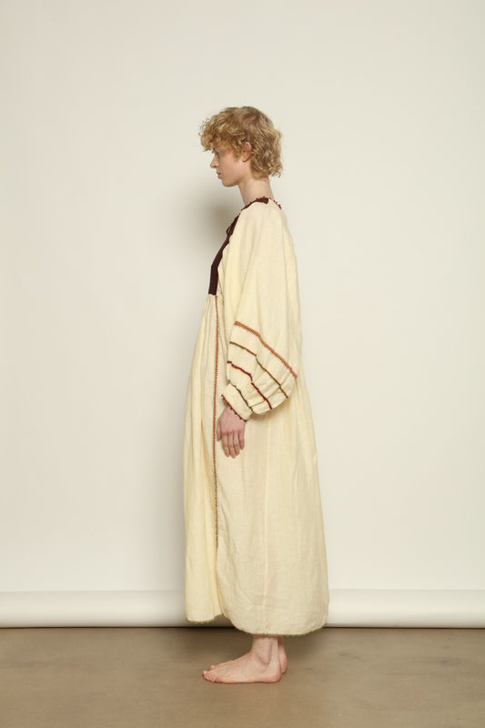 Model is wearing the Serafina Brown Linen Dress by Supernaturae x HONS, crafted in a blend of crisp linen and hand-spun silk with rich earthy botanical dye tones. Featuring a 1970s-inspired kaftan silhouette, hand-crochet edges and adjustable ties, this sustainable slow fashion piece shows natural tonal variations unique to each garment. Made in small-batch production in Mexico using ancestral techniques, part of the House of Woven Stories selection.