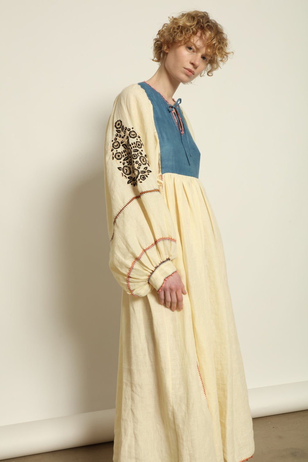 Model is wearing the Serafina Embroidered Blue Linen Dress by Supernaturae x HONS, crafted in a blend of crisp linen and hand-spun silk with deep natural indigo dye tones. This sustainable slow fashion piece features delicate hand embroidery and crochet edges, created through ancestral artisan techniques between India and Mexico. Part of the House of Nomad Stories selection.