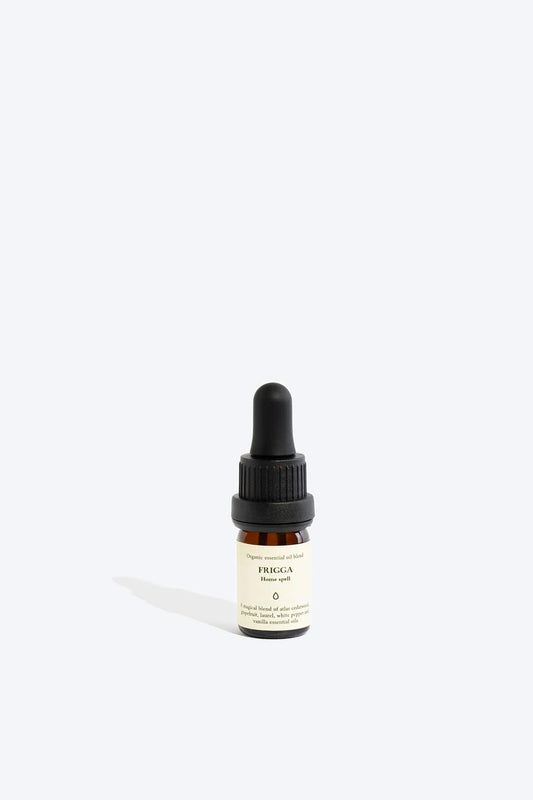 Bottle of Frigga organic essential oil blend by Smells Like Spells, placed on a natural surface with herbs, ideal for home protection and harmony rituals.
