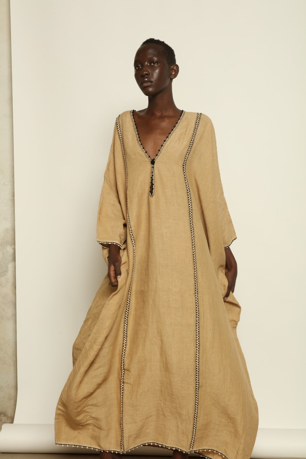 Model is wearing the Thea Beige Linen Dress by Supernaturae x HONS in soft botanical sandy beige linen, featuring a relaxed flowing silhouette, structured breathable fabric and elegant open back design. Part of the House of Woven Stories selection, this ethical slow fashion piece is hand-dyed with natural pigments, showing organic tonal variations.