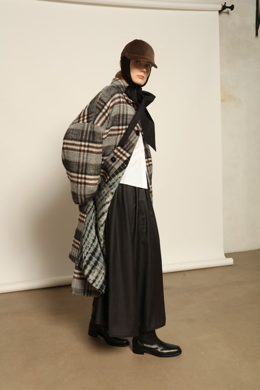 Model is wearing the Tiflis Checked Coat by House of Woven Stories, crafted from a soft wool blend with muted grey and brown checks, featuring an oversized silhouette, wide sleeves, and structured collar for timeless elegance.