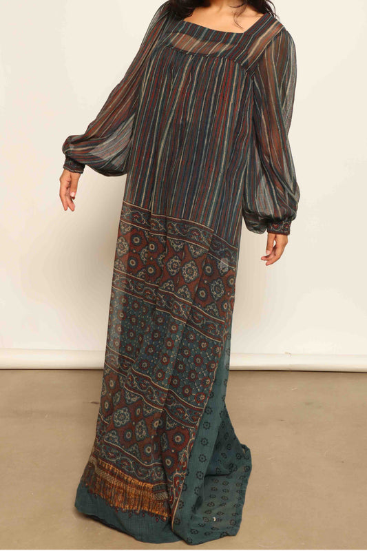 Model is wearing the Woodstock Dark silk dress by House Of Woven Stories, handcrafted in Italy from re-wearable sari fabric, featuring sheer sleeves, handprinted details, and a flowing silhouette.