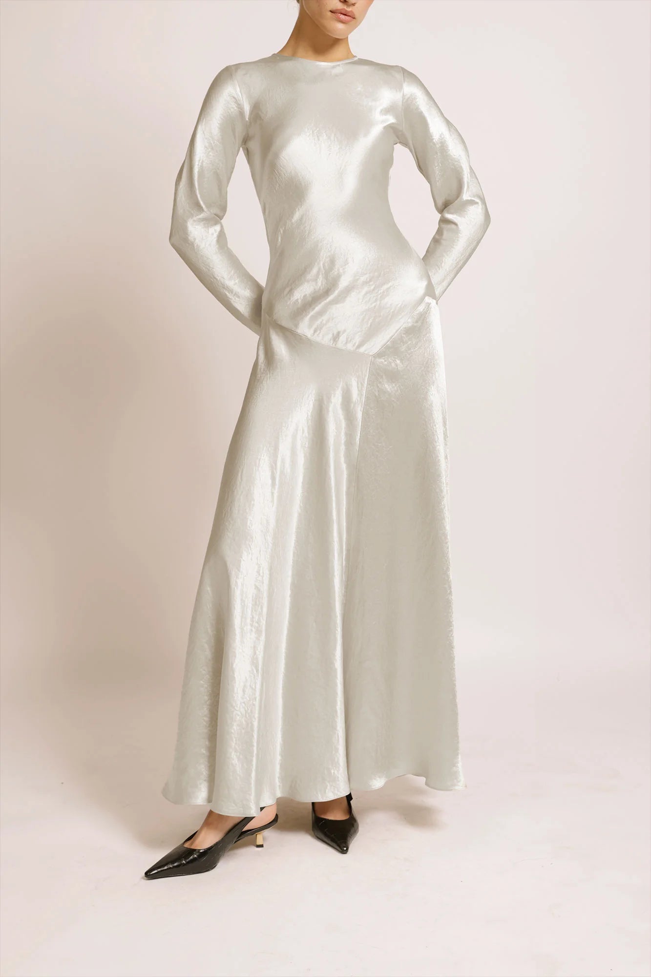 Model wearing a silver silk satin Yara Dress by Abadia from the House of Nomad Stories collection, featuring a bias-cut silhouette, long sleeves, and a fluid elegant drape with a subtle metallic sheen.