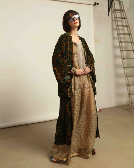 Model is wearing a golden sage silk and velvet abaya with geometric patterns, featuring a flowing elegant silhouette, perfect for modern and regal styling.