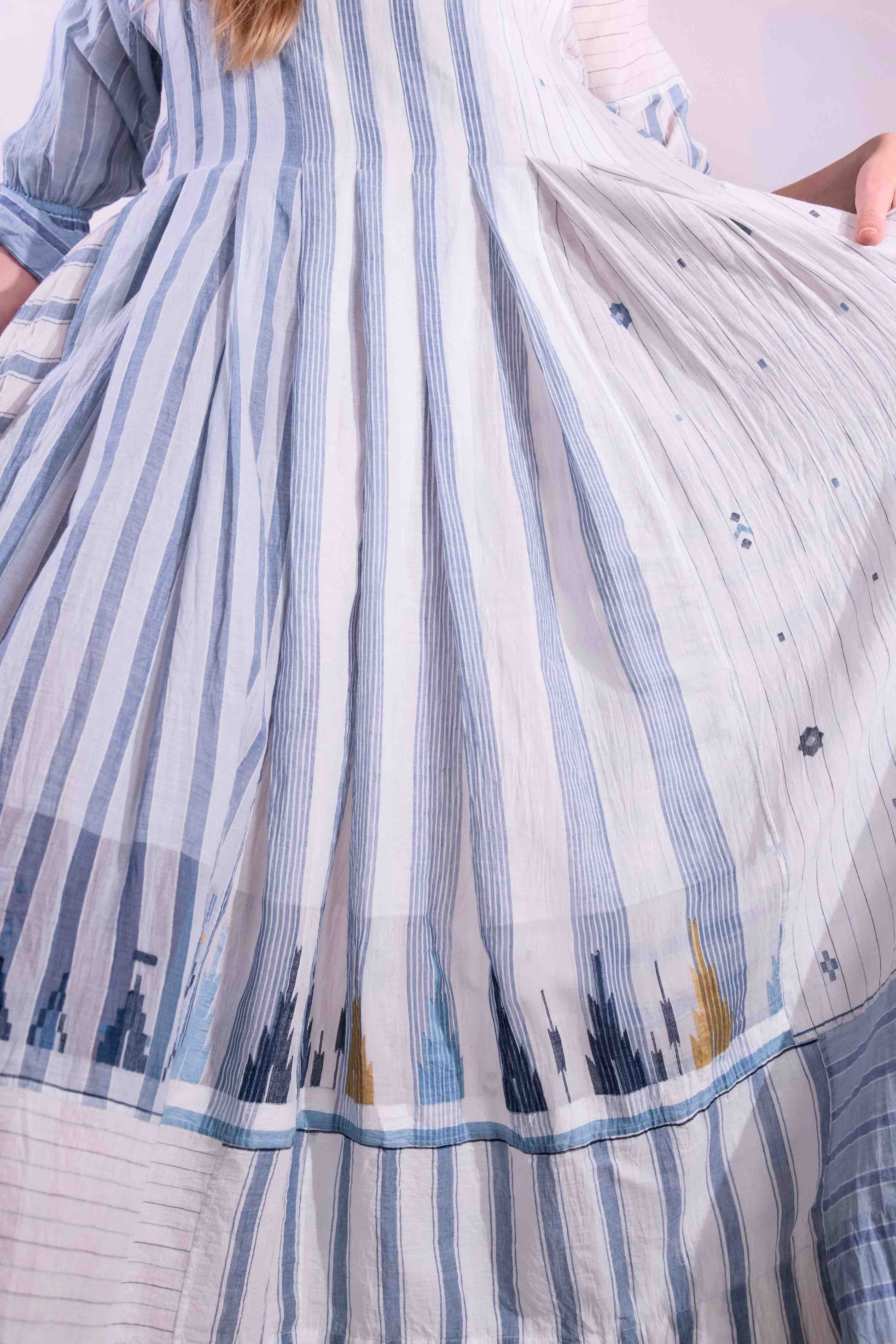 Woven wearing handcrafted pure cotton dress by Injiri in white with blue patterns and delicate embroidery, featuring short sleeves, side pockets, and a relaxed, airy silhouette. Available at House of Woven Stories.