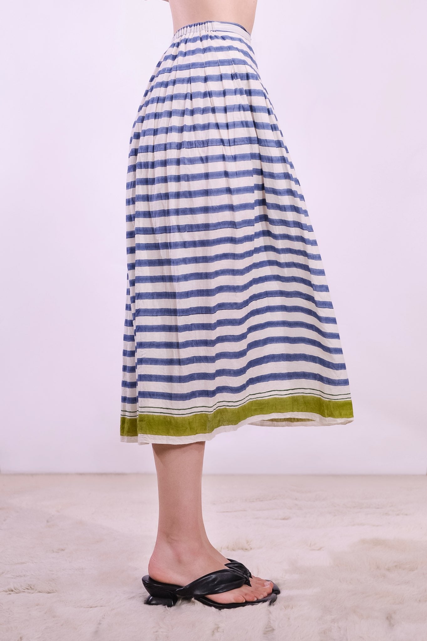 Model wearing a long pleated pure cotton skirt with indigo and off-white stripes, elastic waistband, and pistachio hem. Handcrafted in India by Injiri.