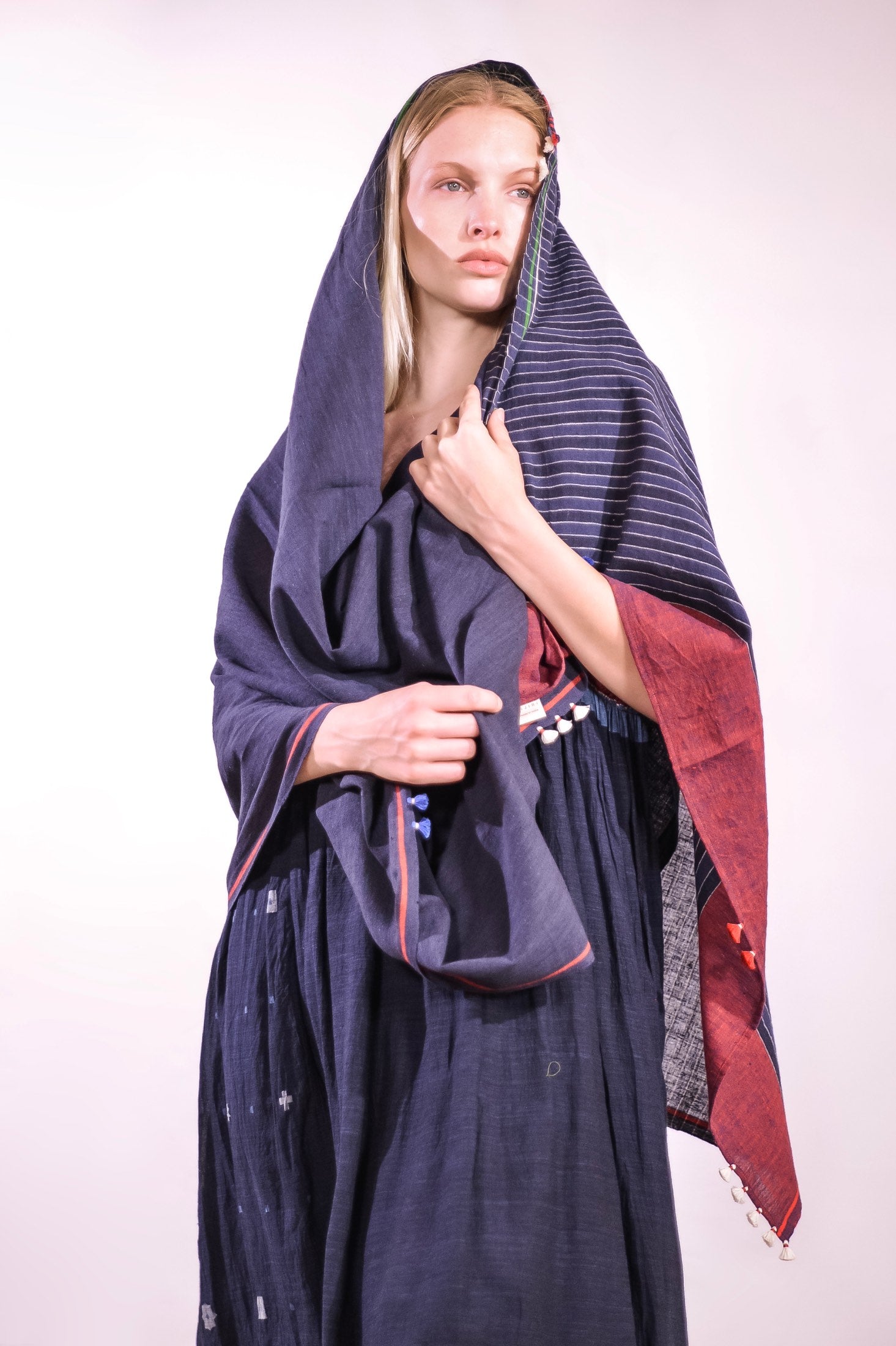 Model wearing pure cotton scarf by Injiri – handloomed unisex accessory in natural indigo with red and white woven details, crafted from organic cotton and finished with tassels. Ethically handmade in India