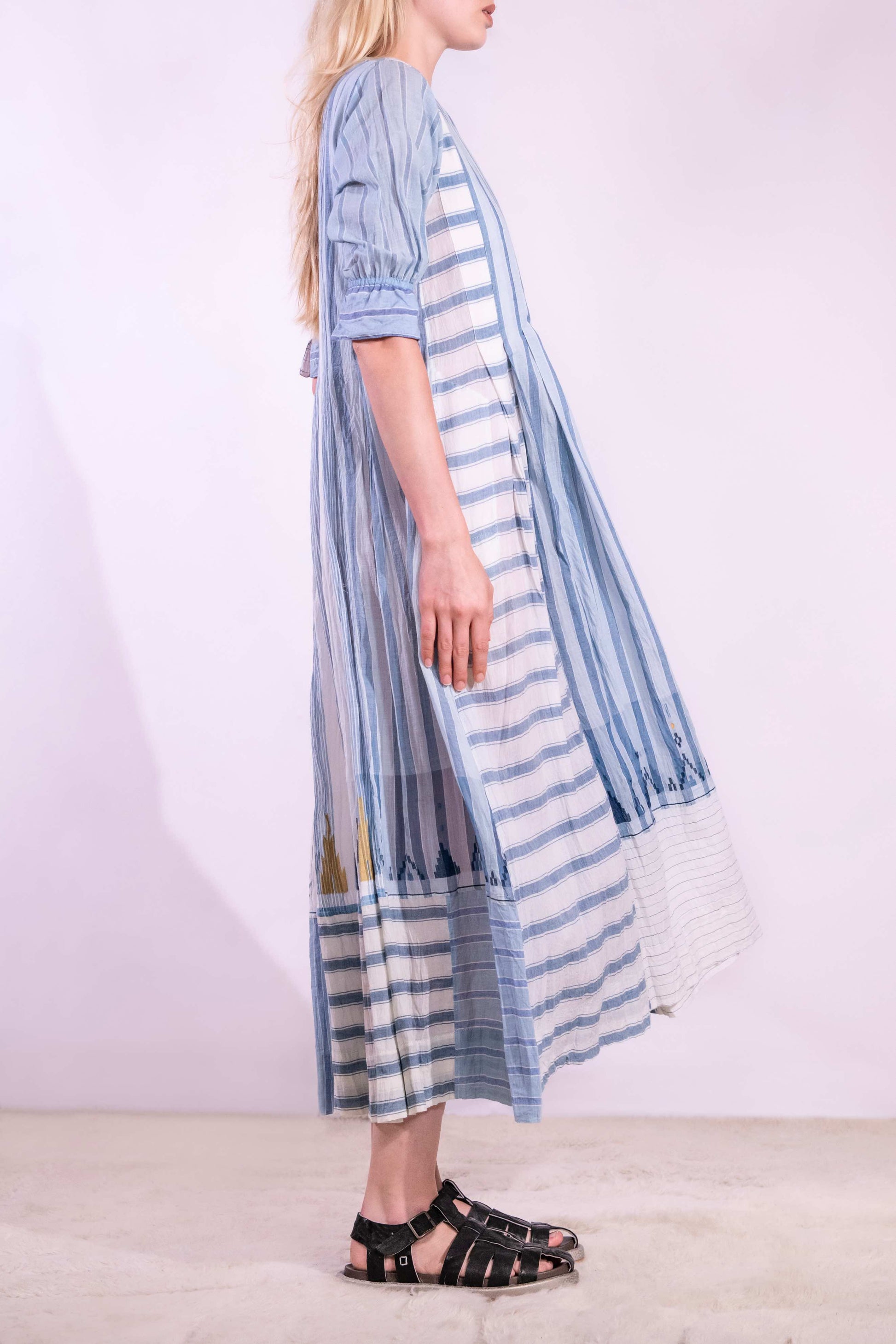 Woven wearing handcrafted pure cotton dress by Injiri in white with blue patterns and delicate embroidery, featuring short sleeves, side pockets, and a relaxed, airy silhouette. Available at House of Woven Stories.