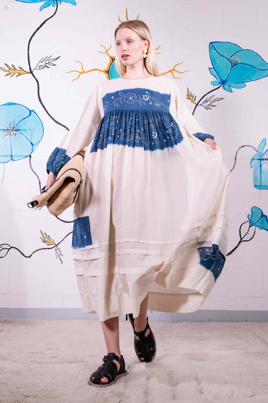 Model wearing pure cotton maxi dress by Injiri – long-sleeve off-white handloomed dress with indigo tie-dye and shibori print, side pockets, and fluid silhouette. Handcrafted in India using organic cotton.