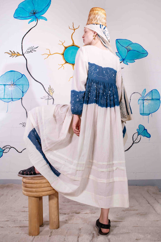 Model wearing pure cotton maxi dress by Injiri – long-sleeve off-white handloomed dress with indigo tie-dye and shibori print, side pockets, and fluid silhouette. Handcrafted in India using organic cotton.
