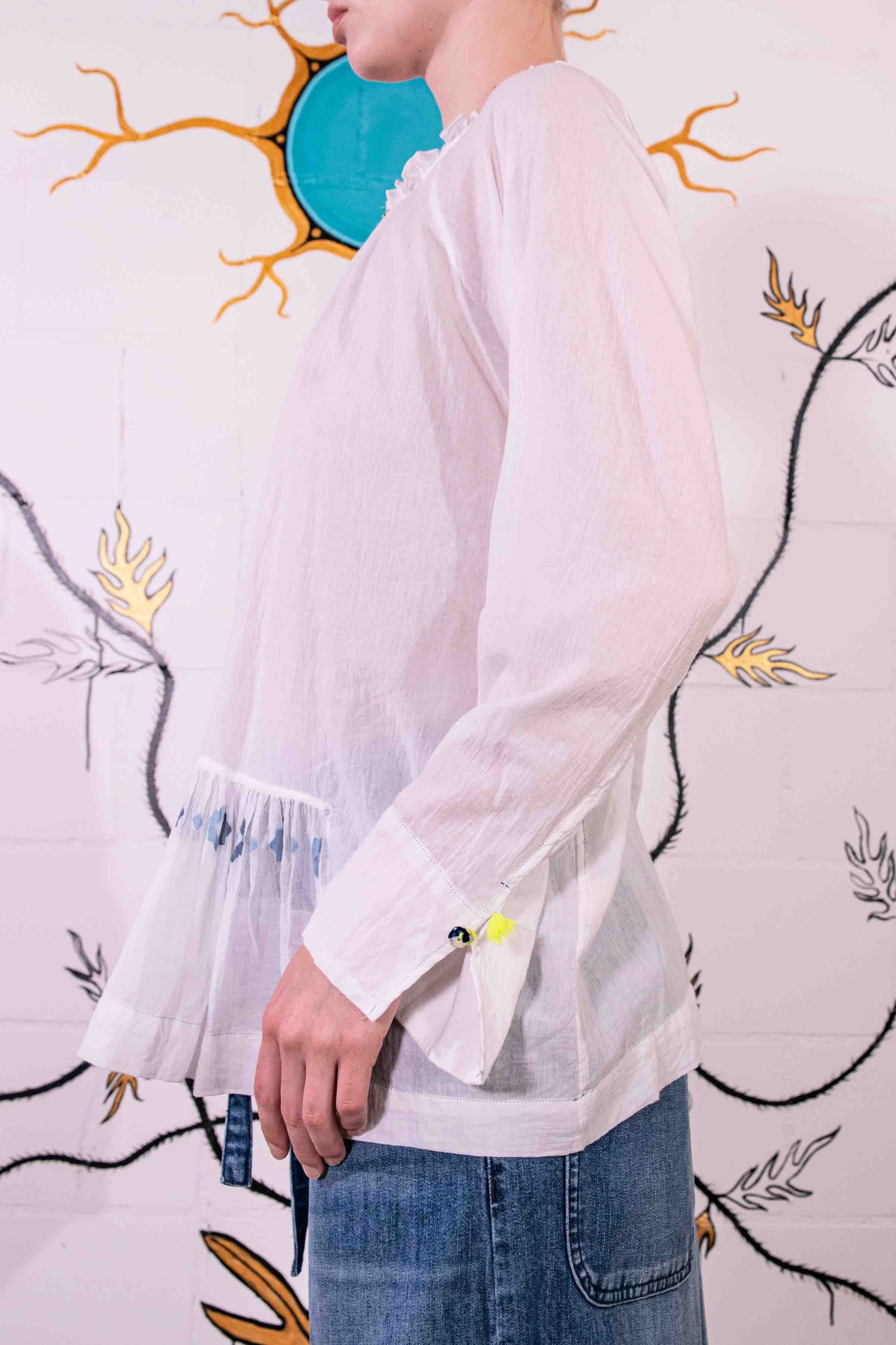 Model wearing Amber 38 pure cotton shirt by Injiri. Long-sleeved white handwoven mousseline cotton shirt with jamdani weaving, stitched detailing, and yellow tassels. Ethically handcrafted in Jaipur, India, and available at House of Woven Stories. 