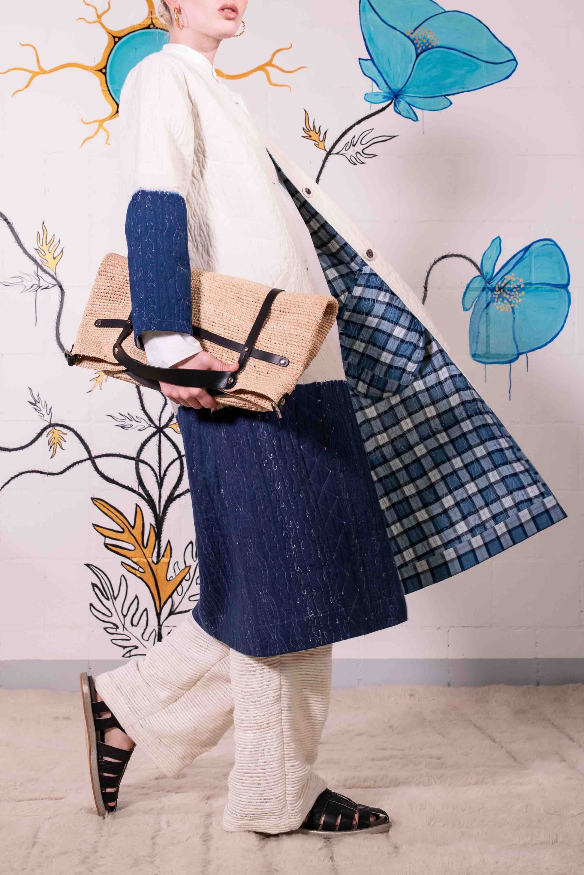 Model is wearing a reversible quilted cotton coat by Injiri, featuring a tie-dye design in off-white and deep indigo, with a split rounded collar, contrast buttons, and blue madras check lining.