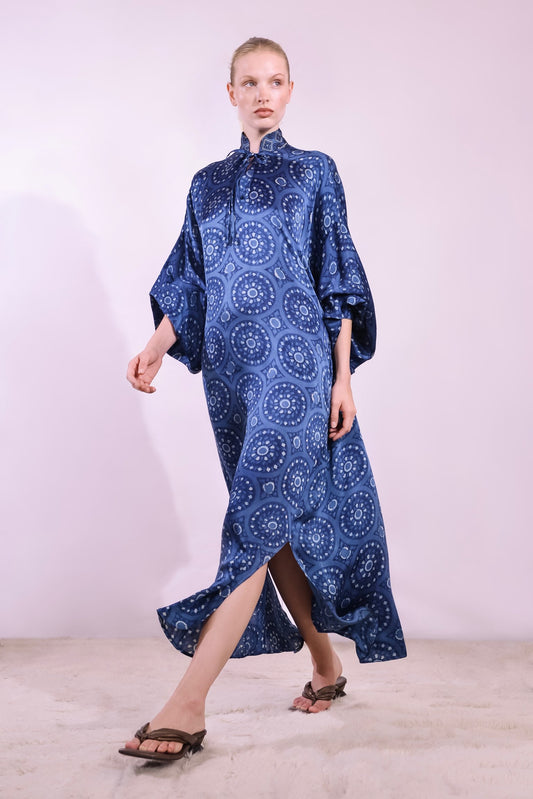 Model wearing Blue Circles Marion Silk Dress by Obidi. Handprinted silk maxi dress with V-neckline, natural indigo Ajrakh blockprint, side pockets, and fluid silhouette. Ethically made in India using traditional techniques.