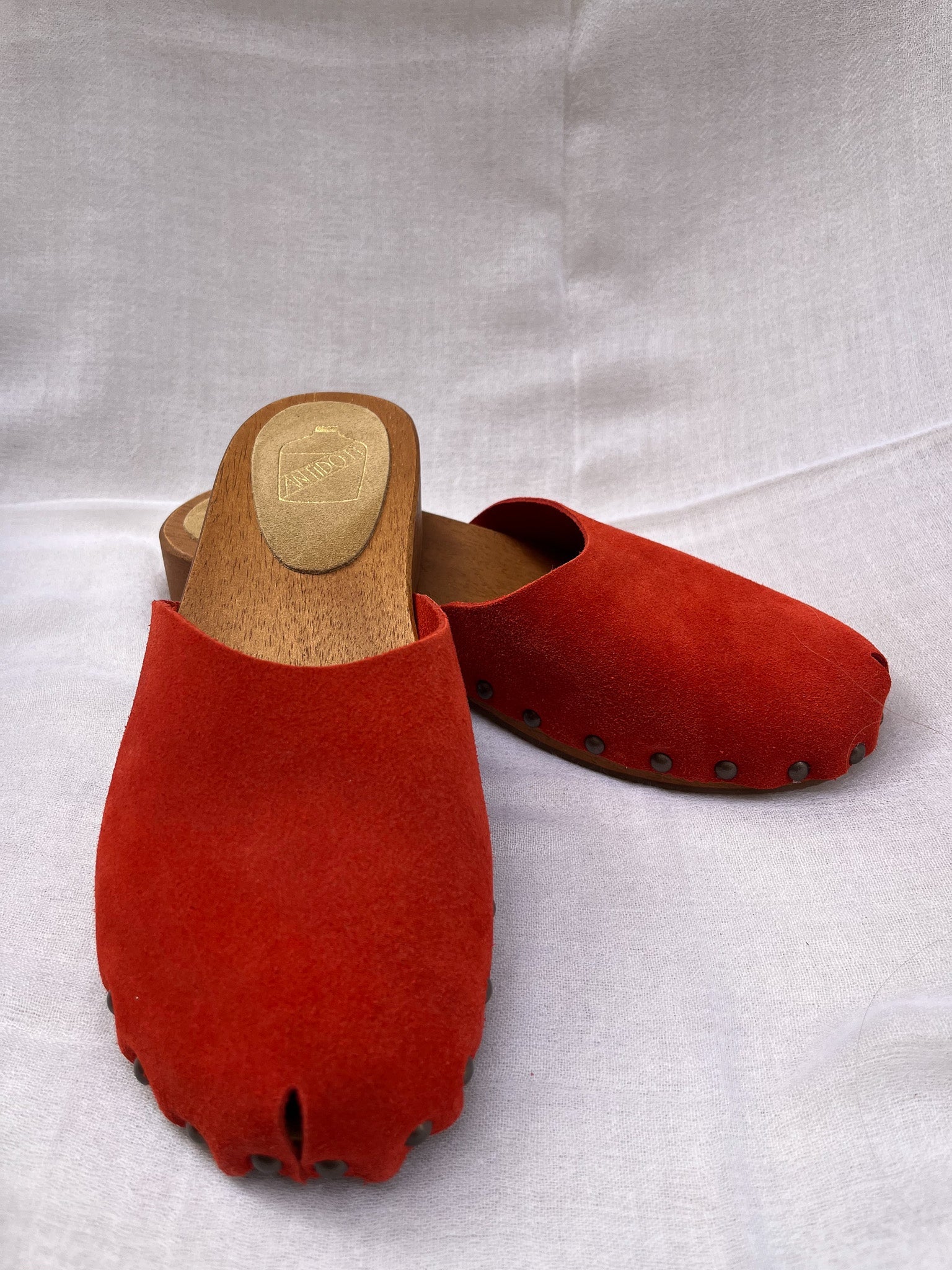 Handmade candy red clogs by Antidoti with studded sides and wooden sole, crafted in Florence, Italy. Available at House of Woven Stories.