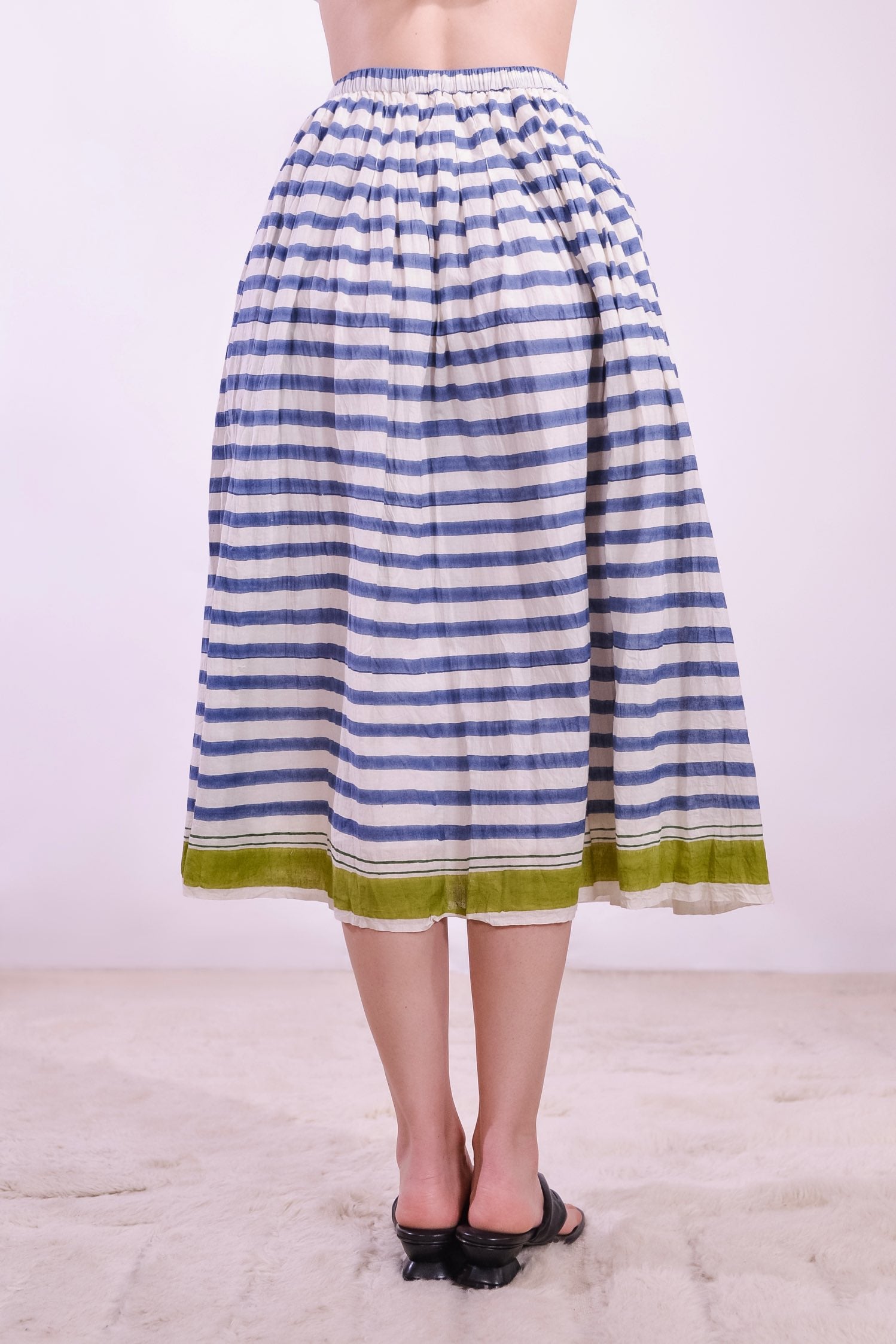 Model wearing a long pleated pure cotton skirt with indigo and off-white stripes, elastic waistband, and pistachio hem. Handcrafted in India by Injiri.