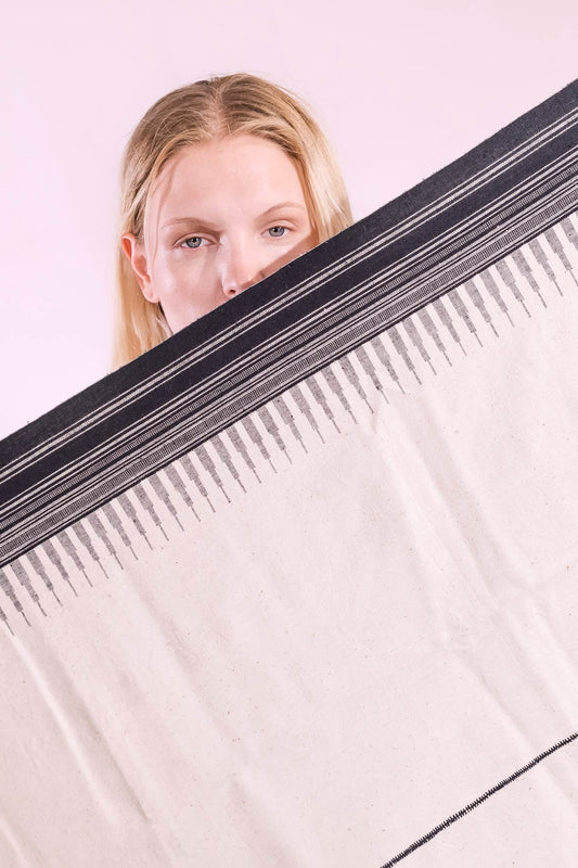 Model is holding the Ananta handwoven kala cotton throw by House of Woven Stories - made from handspun yarn with embroidered panels, crafted in Kutch, India by master weaver Shamji Vankar.
