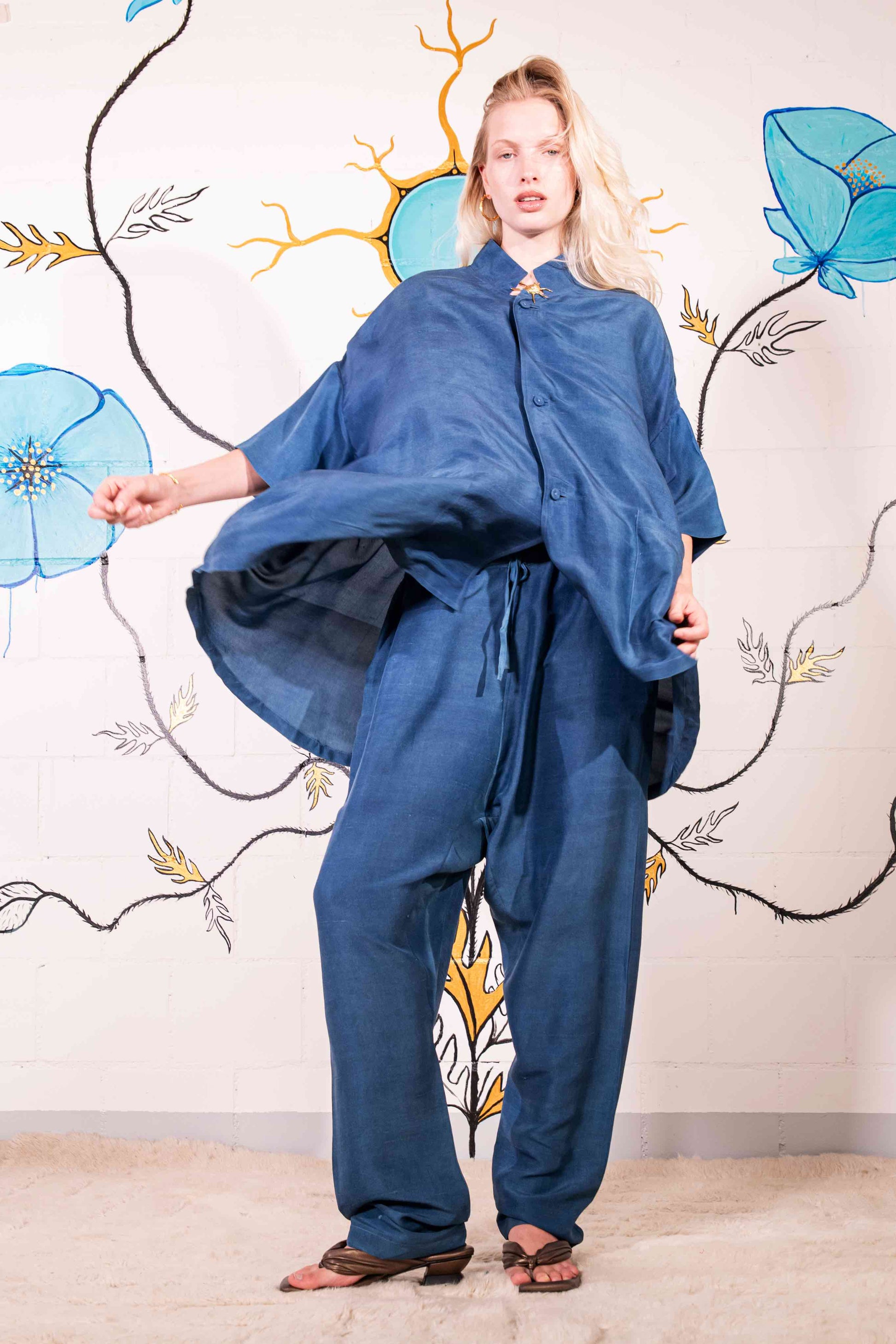 Model is wearing a short-sleeve indigo shirt made from 100% silk, featuring a relaxed fit, dropped shoulders, front button closure, and large patch pockets. Hand-dyed using botanical pigments by A Sacred Wrap.