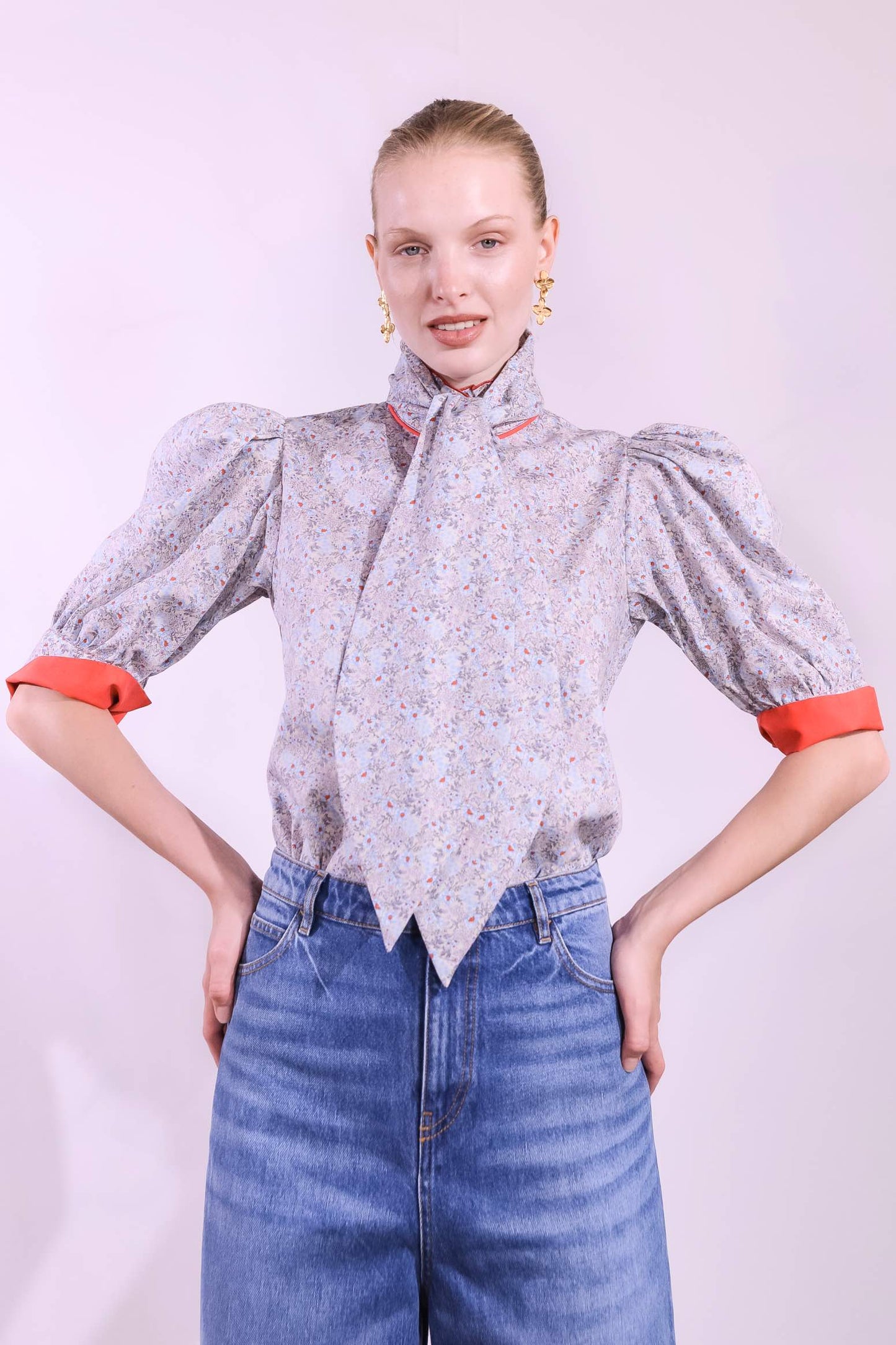 Model is wearing the Mirca Fantasia Liberty Blouse by House of Woven Stories: a lightweight cotton blouse with Liberty floral print, puffed sleeves, bright coral trims, a vintage collar button, and a matching fabric tie for styling.